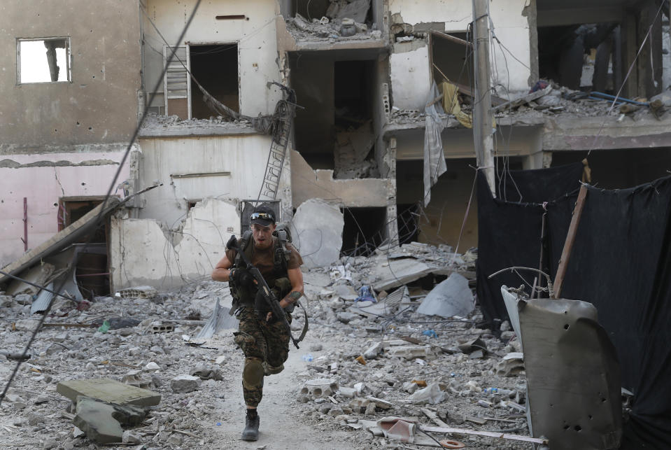 FILE - In this Thursday, July 27, 2017, a U.S.-backed Syrian Democratic Forces fighter runs in front of a damaged building as he crosses a street on the front line, in Raqqa city, Syria. With Islamic State's near total defeat on the battle field, the extremist group has reverted to what it was before its spectacular series of conquests in 2014 _ a shadowy terror network that targets vulnerable civilian populations and exploits state weaknesses to incite on sectarian strife. But a recent surge in false claims of responsibility for attacks also signals that the group is struggling to stay relevant after losing its proto-state and its dominance of the international news agenda. (AP Photo/Hussein Malla, File)