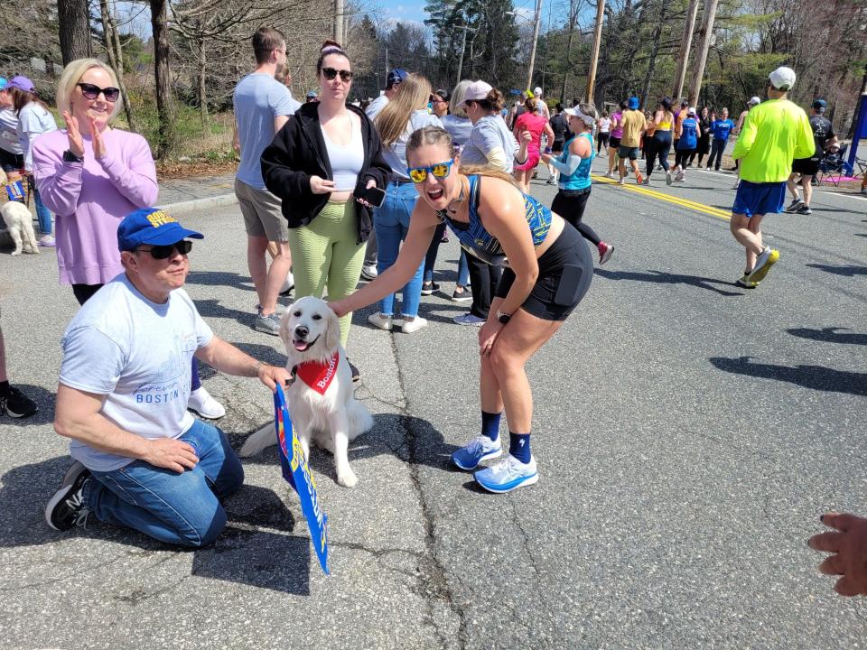 Hannah Sedgwick, right, of Culver City, California, takes a quick break during her Boston Marathon run to greet Jimmy, who is owned by Rich Powers, left, in Ashland. Powers previously owned a golden retriever named Spencer who was honored by the Boston Athletic Association as the "official dog of the Boston Marathon."