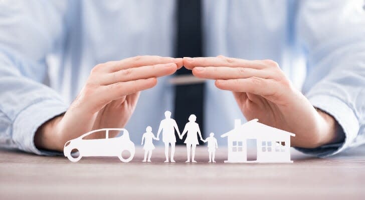 Man's hands held over paper cutouts of a car, a familiy and a house