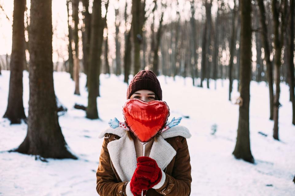 young happy woman in winter sunny day holding red funny balloon in shape of heart concept of 14th of february, valentine's day, love and relationship