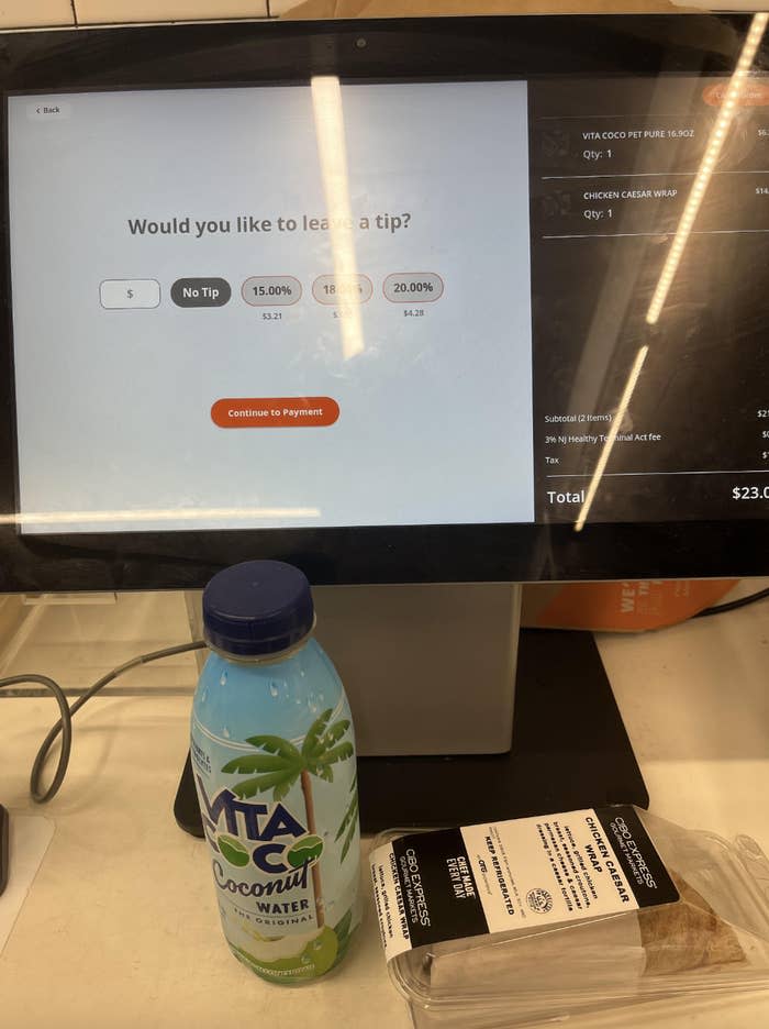 Digital payment screen asking for a tip with options, with a bottle of coconut water and wrapped pastry on the counter