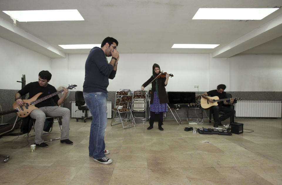 In this picture taken on Friday, Feb. 1, 2013, Kamyar Shahdoust with base guitar, from left, Danial Izadi with harmonica, Nastaran Ghaffari with violin and Hamed Babaei with electric guitar, members of an Iranian band called "Accolade," practice in a basement of a house in Tehran, Iran. Headphone-wearing disc jockeys mixing beats. It’s an underground music scene that is flourishing in Iran, despite government restrictions. (AP Photo/Vahid Salemi)