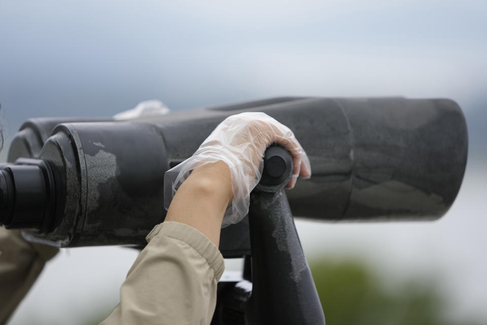 A visitor wearing plastic gloves to help protect against the spread of the coronavirus holds binoculars to see the North Korean side from the unification observatory in Paju, South Korea, Tuesday, Sept. 28, 2021. (AP Photo/Lee Jin-man)