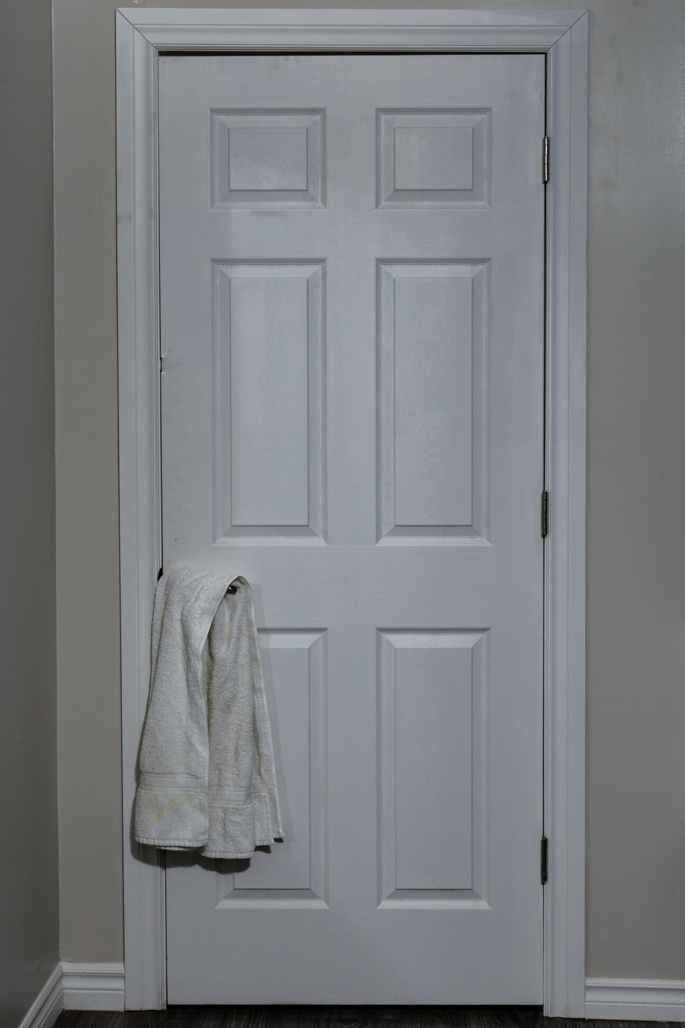A closed white door with six panels has a white bath towel hanging on the handle. There are no people or other objects in the image