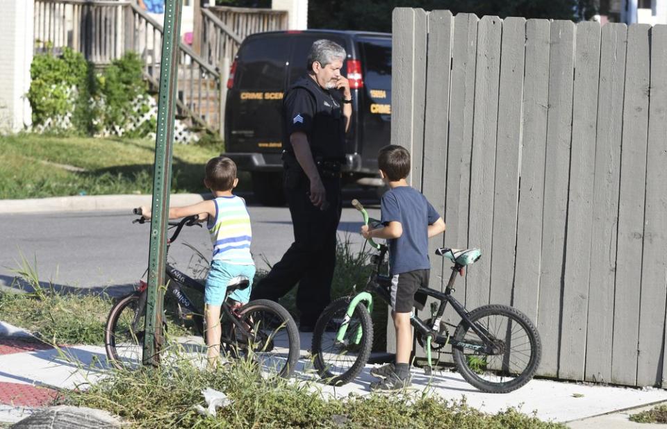 Two boys watch as a Detroit police officer investigates a fatal dog attack on a young girl who later died of her injuries in Detroit on Monday, Aug. 19, 2019. Police say the owner of three dogs is in custody after the animals killed Emma Hernandez, 9, as she rode a bike. The girl's father, Armando Hernandez, says the man was warned that a fence was too flimsy to hold the dogs. (Max Ortiz/Detroit News via AP)