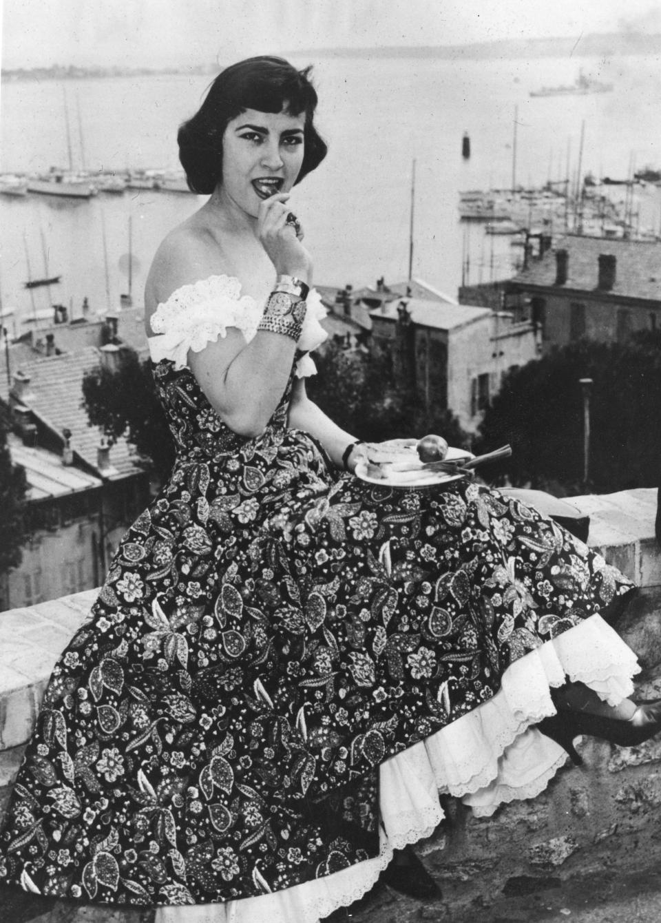 Greek actress Irene Papas, sits on a wall at the harbor of Cannes, France, where she enjoys a solitary lunch, visiting the 7th International Film Festival here, April 6, 1954. Greek actress and recording artist Irene Papas who stared along side Hollywood greats acting alongside Hollywood stars Gregory Peck, Anthony Quinn and Kirk Douglas, died Wednesday, Sept. 14, 2022, at the age of 93. (AP Photo/Traverso, File)