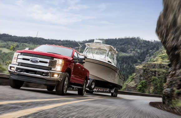 A red 2018 Ford F-250 Lariat, a big pickup truck, is shown towing a boat trailer up a mountain road.