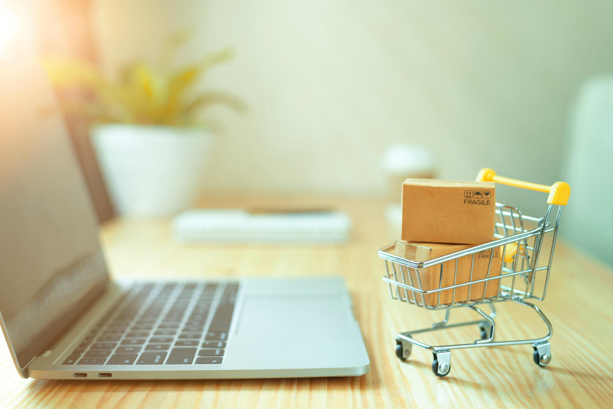 Brown paper boxs in a shopping cart with laptop keyboard on wood - Credit: Adobe Stock/chaiwat