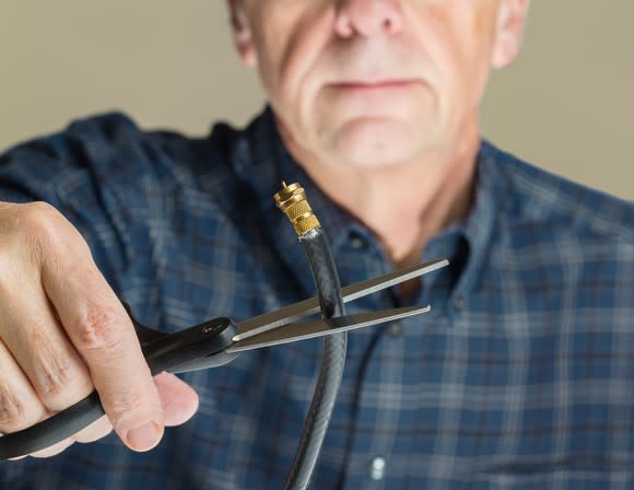 A man cutting a cable cord with scissors.