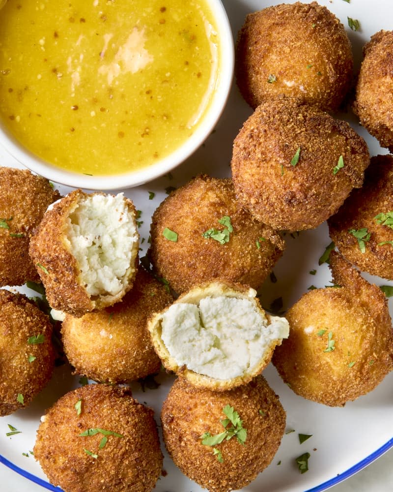 overhead shot of a plate of fried goat cheese balls, with a side of mustard dipping sauce, and on e of the balls is pulled apart.