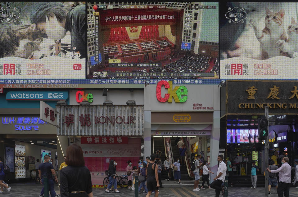 Pedestrians walk under a giant screen showing live telecast of the closing session of the National People's Congress, top center, in Hong Kong, Thursday, May 28, 2020. China’s ceremonial legislature on Thursday endorsed a national security law for Hong Kong that has strained relations with the United States and Britain. (AP Photo/Vincent Yu)