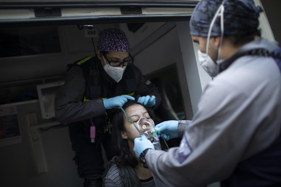 Wearing masks as a precaution against the new coronavirus, Angels of the Road volunteer paramedics Rodolfo Alvarado, right, and Zully Rodiz, place an oxygen mask on a woman who was in a residential building when a car burst into flames in the parking lot, in Caracas, Venezuela, Monday, Feb. 8, 2021. Despite receiving no paychecks, the roughly 40 volunteer paramedics are ready at a moment's notice to jump onto motorcycles and fire up their single ambulance and race into the streets to attend an emergency. (AP Photo/Ariana Cubillos)