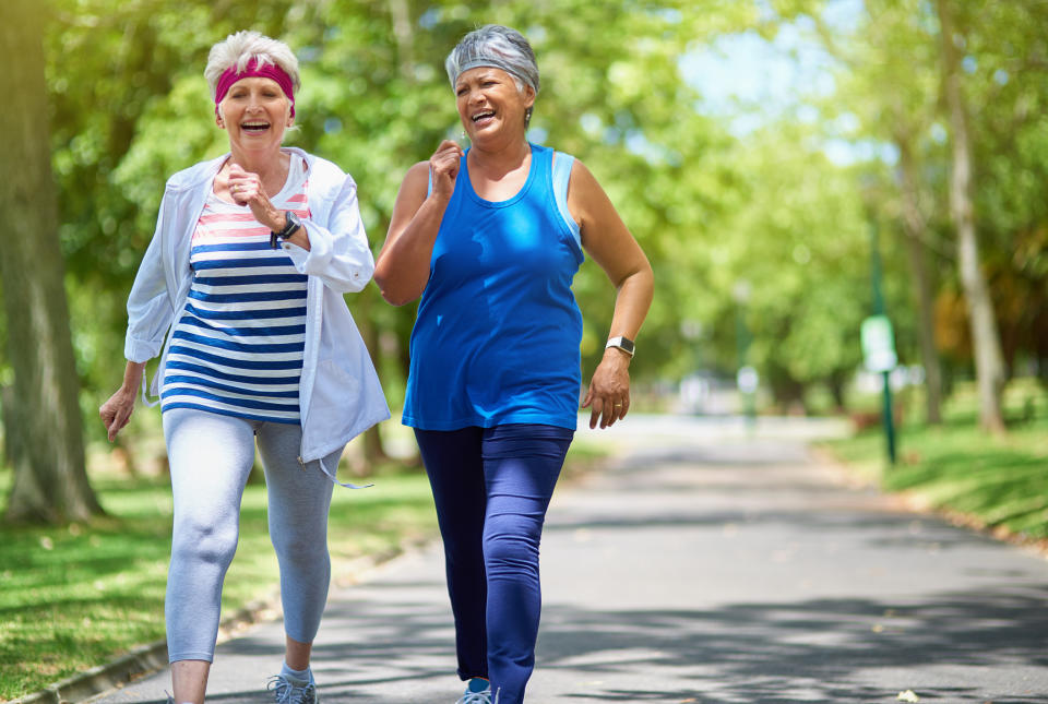 Two older women joyfully power-walking in a park, both in athletic clothing and headbands