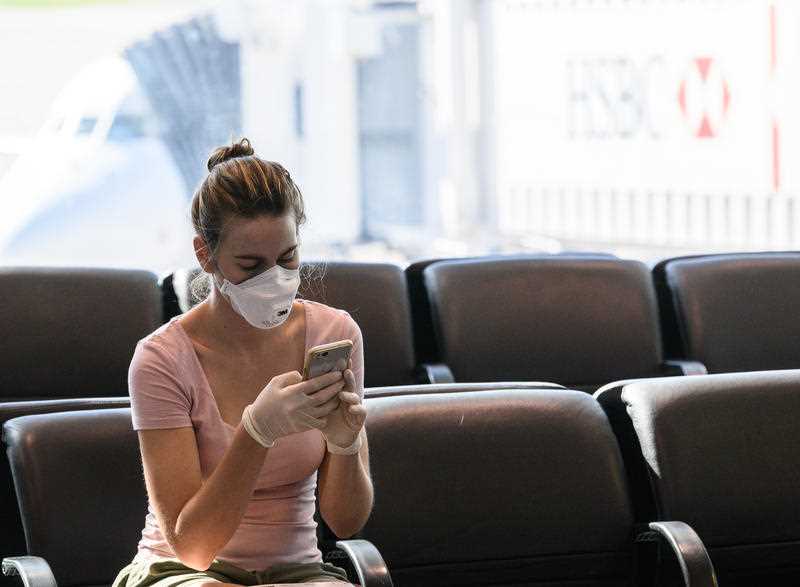 A woman wearing a face mask and gloves looks at her phone at Sydney Airport.