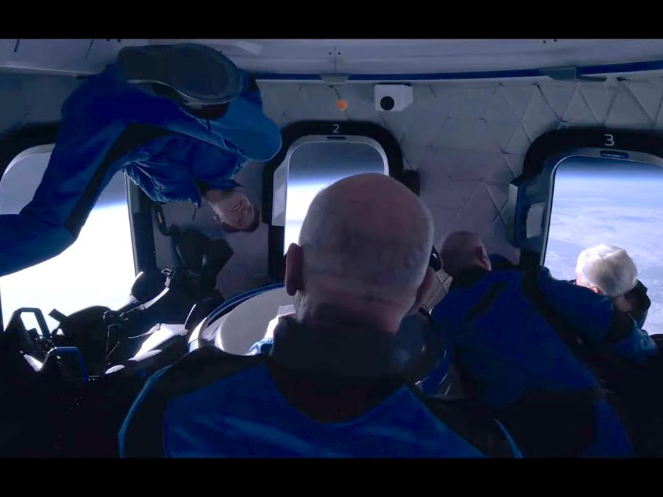 jeff bezos and three other passengers in jumpsuits float around spaceship cabin earth in background