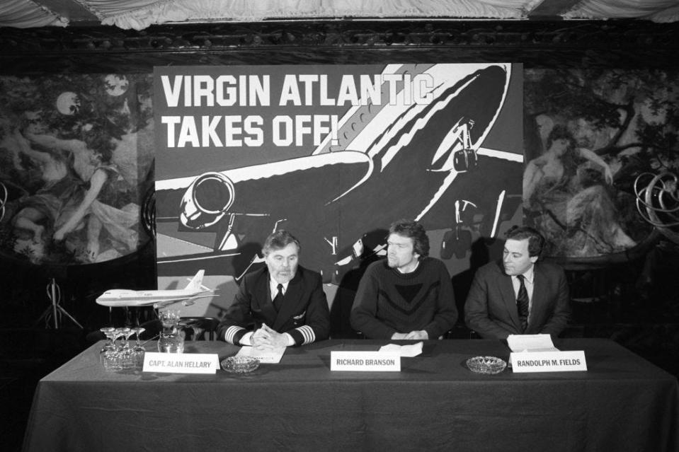 Captain Alan Hellary, Sir Richard Branson, and Randolph Fields at a press conference announcing the launch of Virgin Atlantic Airways in February 1984, sitting behind a table and in front of a sign that reads "Virgin Atlantic Takes Off!"