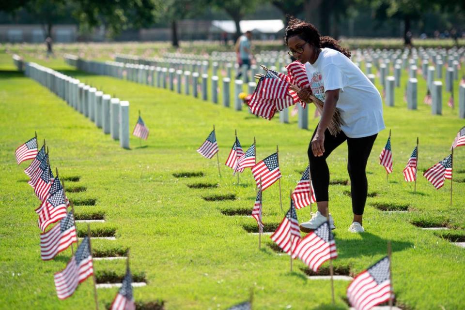 Volunteers help place thousands of tiny American flags on the graves of American service members at Biloxi National Cemetery in Biloxi ahead of Memorial Day on Saturday, May 25, 2024.