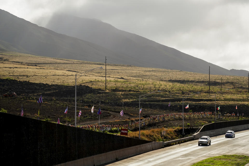 Cars pass by a memorial for victims of the August wildfire, Wednesday, Dec. 6, 2023, above the Lahaina Bypass highway in Lahaina, Hawaii. The wildfire that tore through the heart of the Hawaii island of Maui this summer showed how older residents are at particular risk from disasters. Sixty of the 100 people killed in the Maui fire this summer were 65 or older. (AP Photo/Lindsey Wasson)