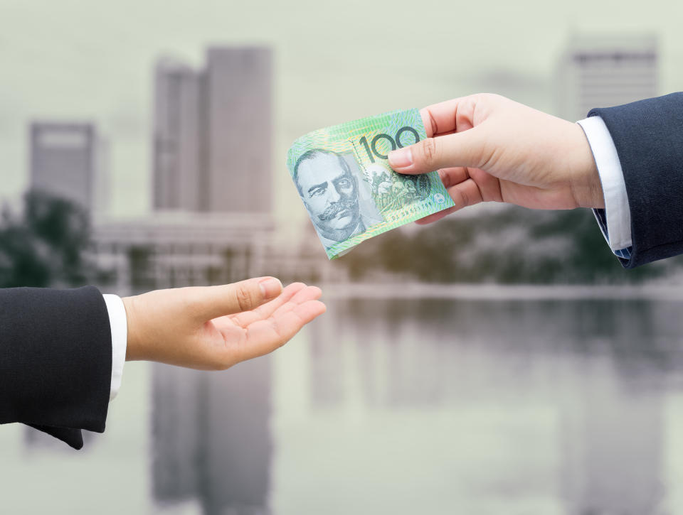 Hands of businessman passing Australian money to another hand. (Source: Getty)