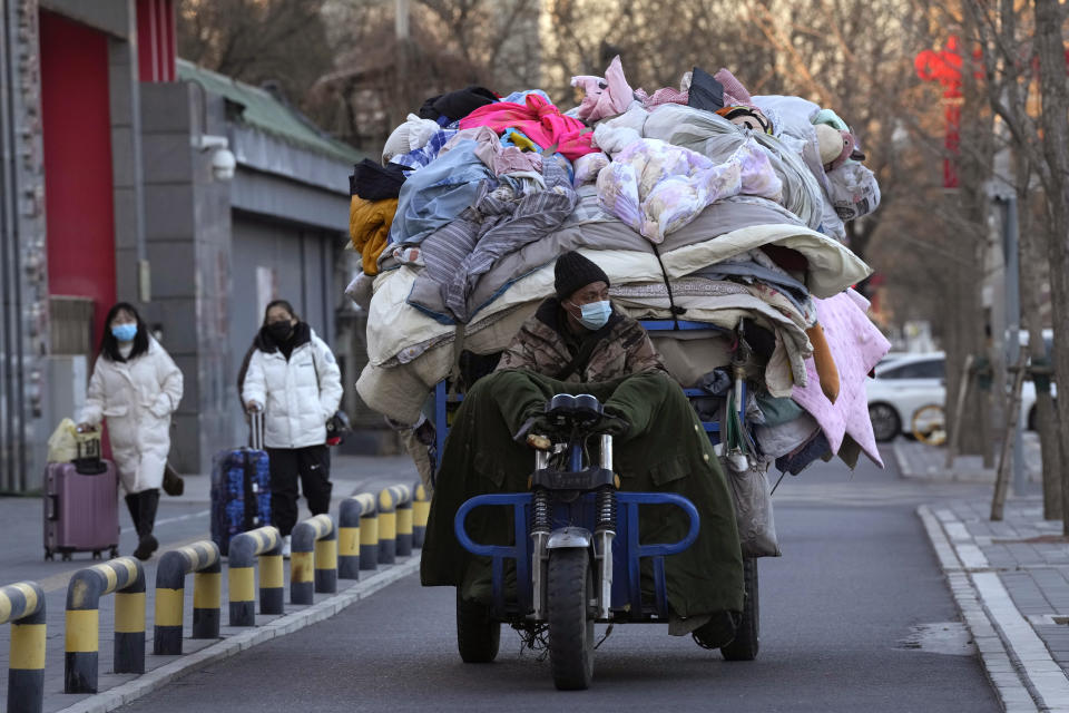 A man wearing a mask transports used quilts and other scavenged cloth material in Beijing, Friday, Dec. 30, 2022. China is on a bumpy road back to normal life as schools, shopping malls and restaurants fill up again following the abrupt end of some of the world's most severe restrictions even as hospitals are swamped with feverish, wheezing COVID-19 patients. (AP Photo/Ng Han Guan)