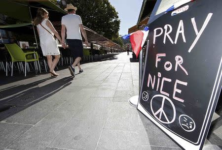 A couple walk through the empty flower market in the old city and near a sign which reads, "Pray for Nice" days after a truck attack on the Promenade des Anglais on Bastille Day killed scores and injured as many in Nice, France, July 17, 2016. REUTERS/Eric Gaillard