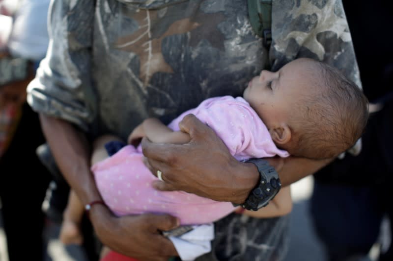 A migrant, part of a group that is mainly from Central America and that travels in a caravan, carries a child as he walks on a road near Frontera Hidalgo, Chiapas