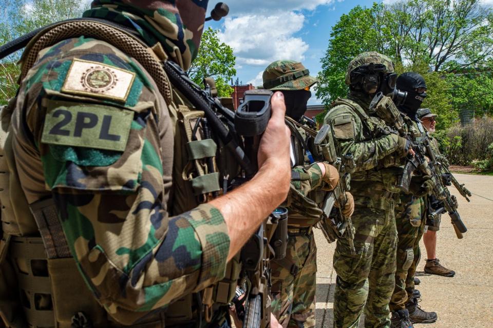 People wearing camouflage, face masks and helmets stand with weapons