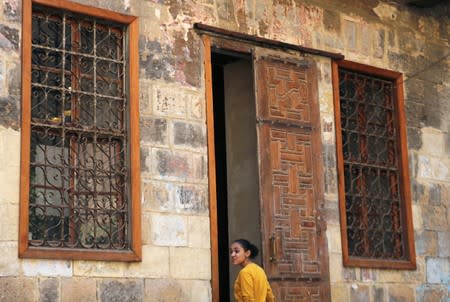 A young woman stands in front of an old wooden door by a historic house in Darb al-Ahmar neighbourhood in Cairo