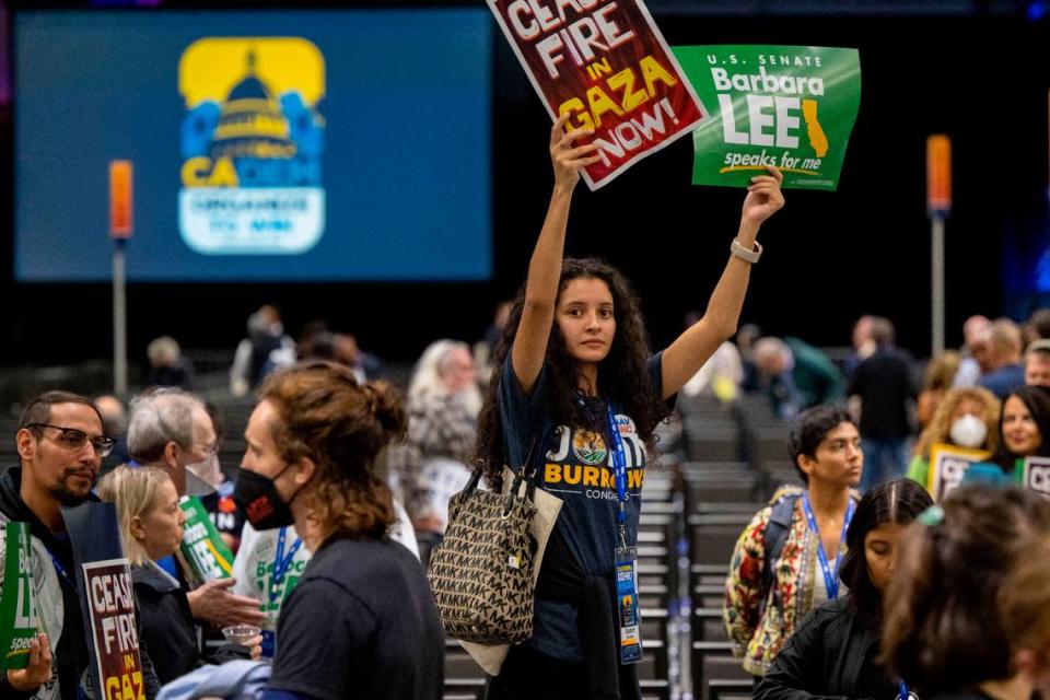 Annamarie Beltran of the Fresno County Young Democrats holds up signs calling for a cease-fire in the Gaza Strip as demonstrators march inside the session at the Democratic nominating convention Saturday at SAFE Credit Union Convention Center in Sacramento.