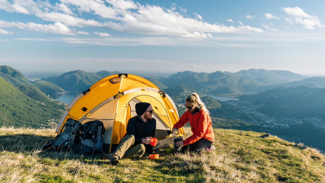  Couple camping on mountain top, preparing food and drinks next to tent. 