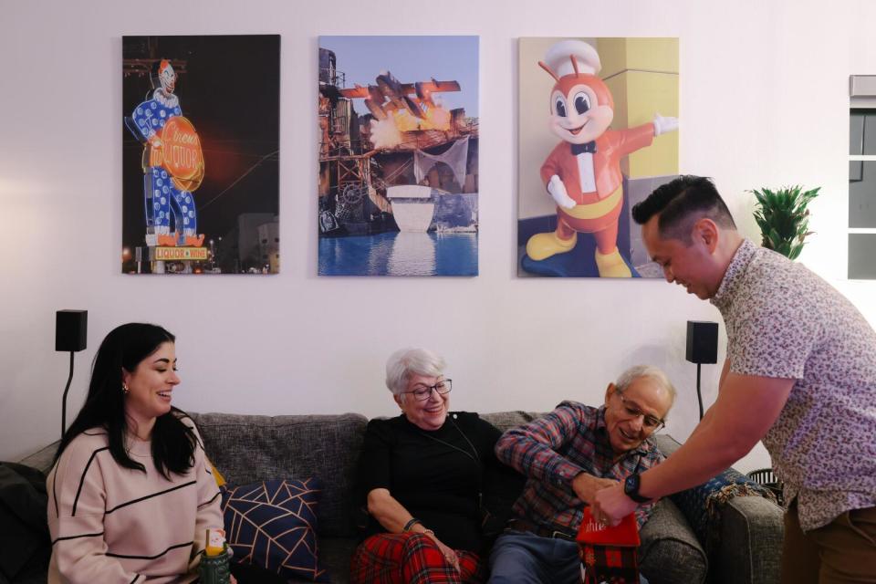 One man stands near another who is sitting on a sofa along with two women.