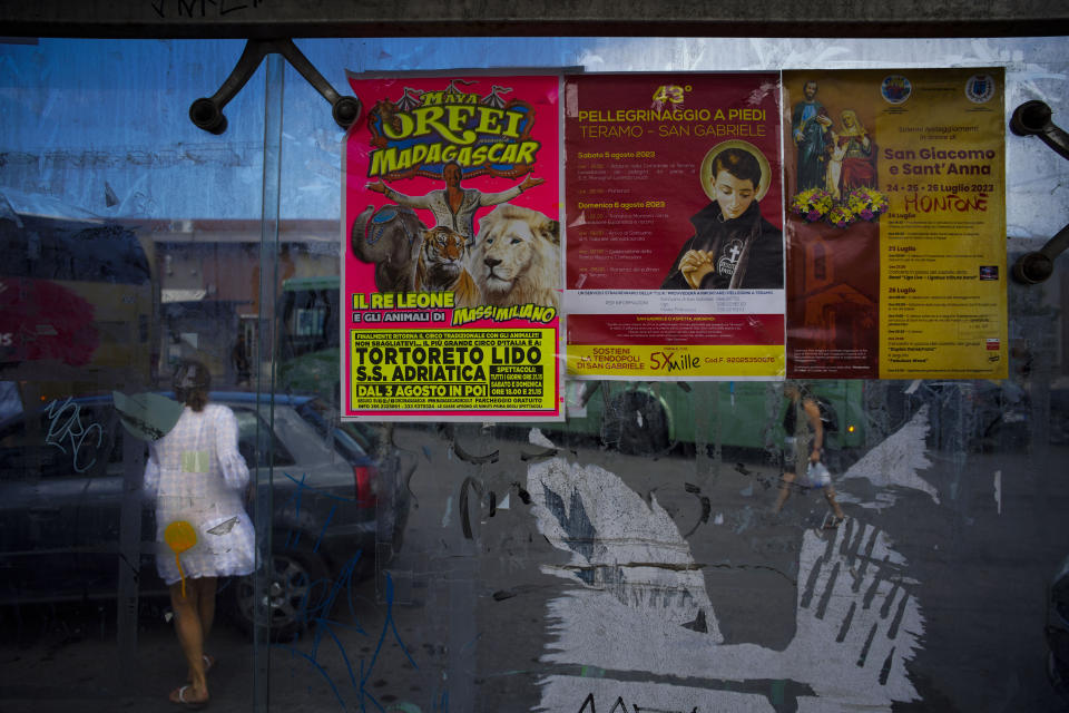 Posters, from left, advertising a show of the Orfei Circus, a 30-kilometer (19-mile) nighttime procession to the St. Gabriele dell'Addolorata sanctuary near Teramo in central Italy, and a local religious festival, hang at a bus shelter by the train station in Giulianova, a nearby resort, Saturday, July 30, 2023. (AP Photo/Domenico Stinellis)