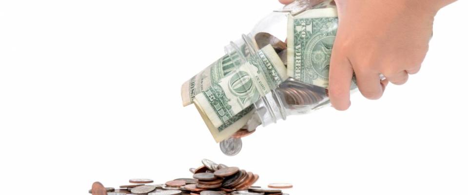 hands shaking money out of glass jar isolated on white background