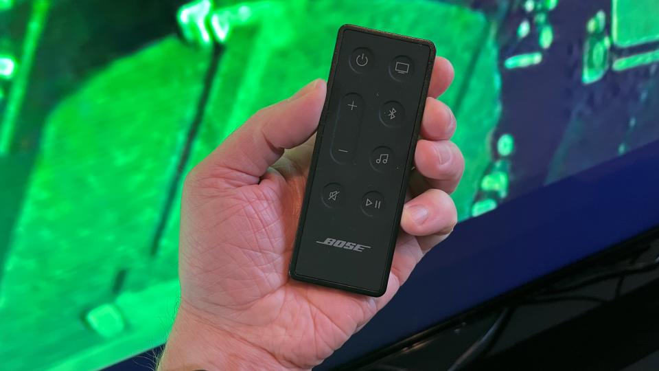 Bose Soundbar 600 remote control held in hand against green background
