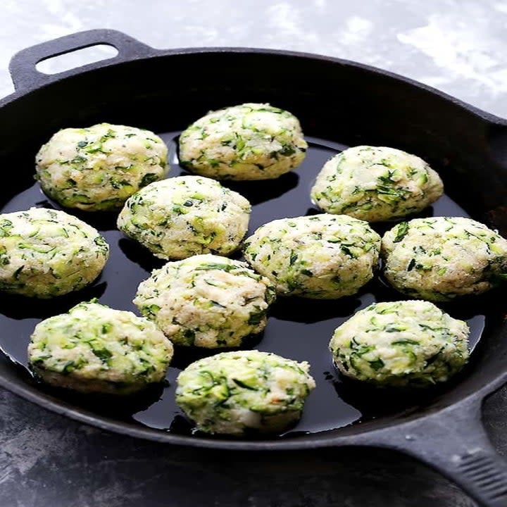 Zucchini and ricotta meatballs cooking in a cast iron skillet.