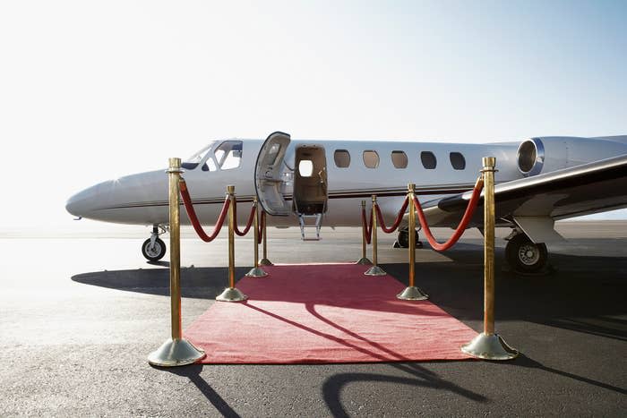 A private jet with its door open, a red carpet laid out leading to the entrance, flanked by gold posts with red ropes