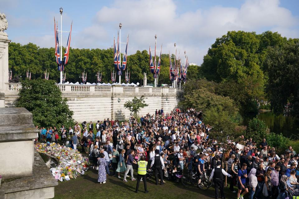 Well-wishes stand beside floral tributes a stone’s throw from the palace. (PA)