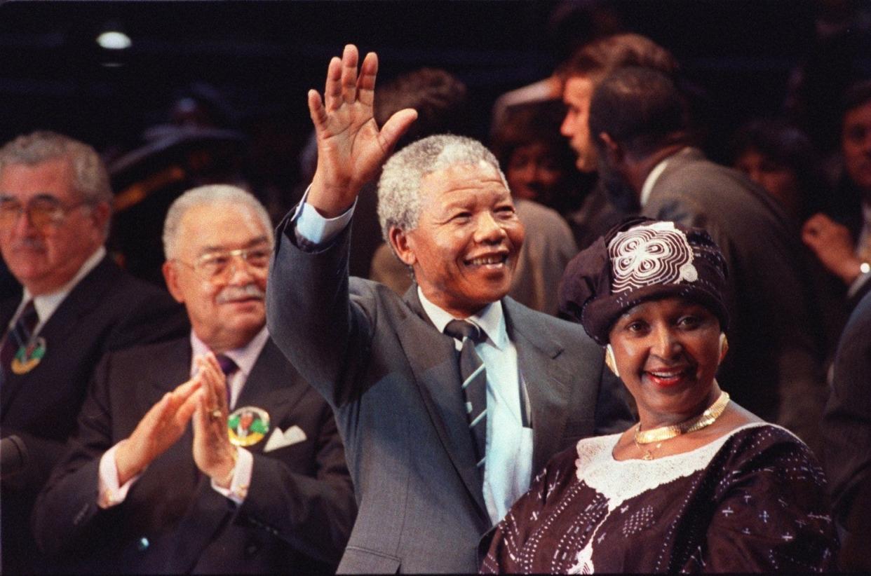 Mayor Coleman Young applauds in the background as Nelson Mandela waves to the crowd with his wife, Winnie, on June 28, 1990.