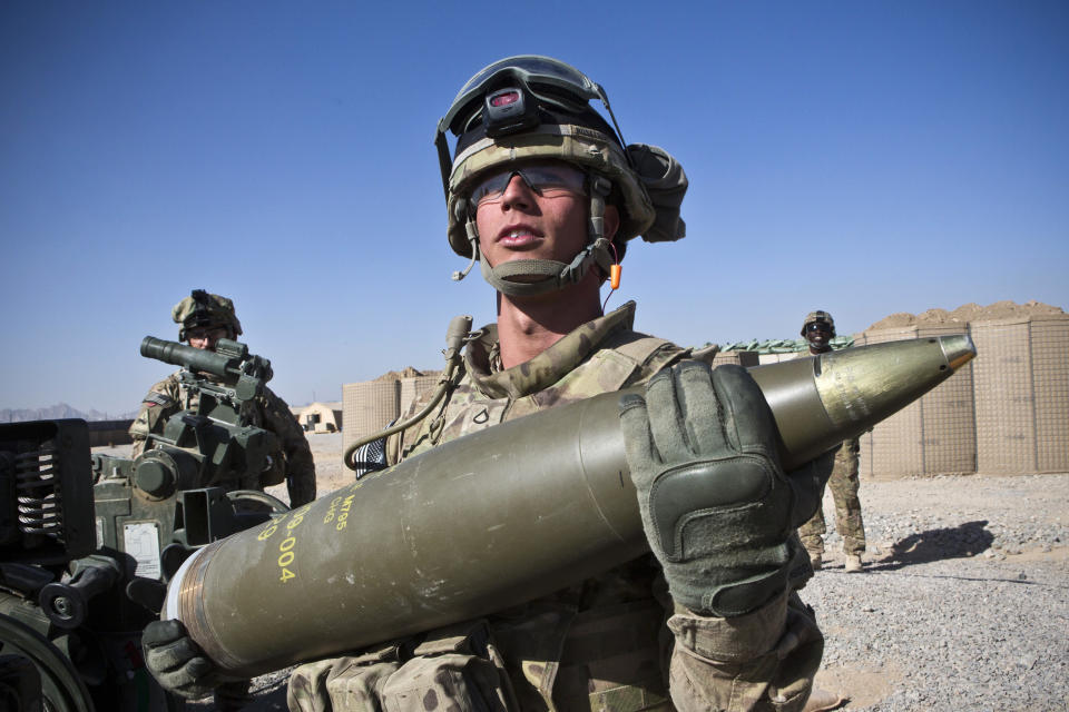 A U.S. Army soldier carrying a 155 mm mortar round.
