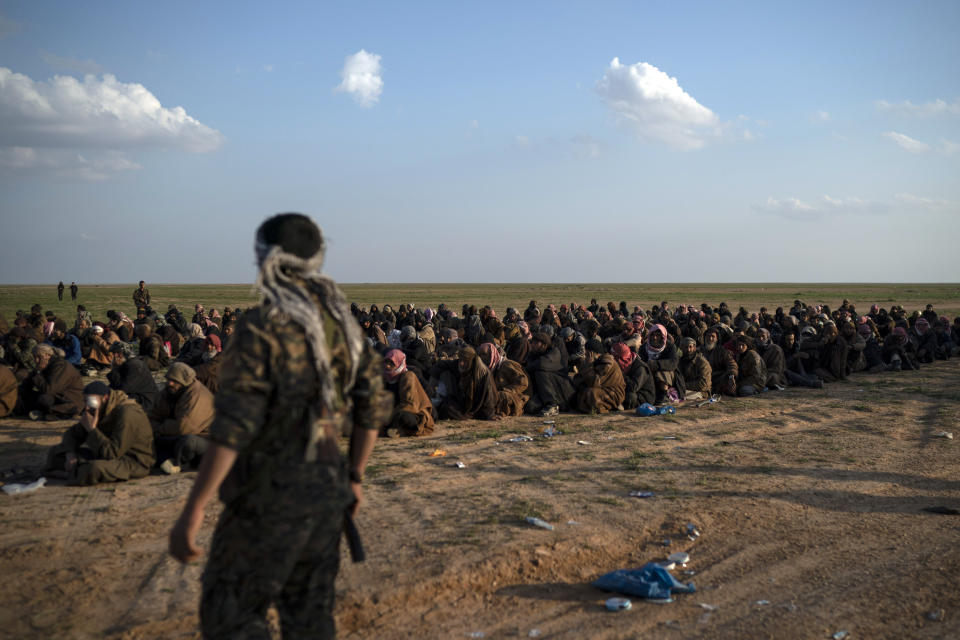 FILE - In this Feb. 22, 2019 file photo, U.S.-backed Syrian Democratic Forces (SDF) fighters stand guard next to men waiting to be screened after being evacuated out of the last territory held by Islamic State group militants, near Baghouz, eastern Syria. The IS erupted from the chaos of Syria and Iraq's conflicts and swiftly did what no Islamic militant group had done before, conquering a giant stretch of territory and declaring itself a "caliphate." U.S. officials said late Saturday, Oct. 26, 2019 that their shadowy leader Abu Bakr al-Baghdadi was the target of an American raid in Syria and may have died in an explosion. (AP Photo/Felipe Dana, File)