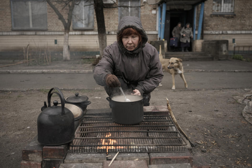 FILE - A woman cooks on an open fire outside an apartment building which according to residents has had no gas, water, electricity and heating for more than a month in the formerly Russian-occupied Kyiv suburb of Bucha, Ukraine, April 2, 2022. The scenes that emerged from this town near Kyiv a year ago after it was retaken from Russian forces have indelibly linked its name to the savagery of war. (AP Photo/Vadim Ghirda, File)