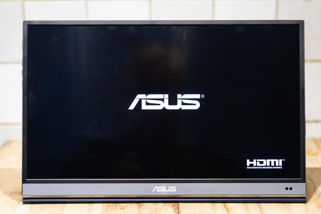  A black and silver ASUS ZenScreen MQ16AH portable monitor on a wooden brown desk. 