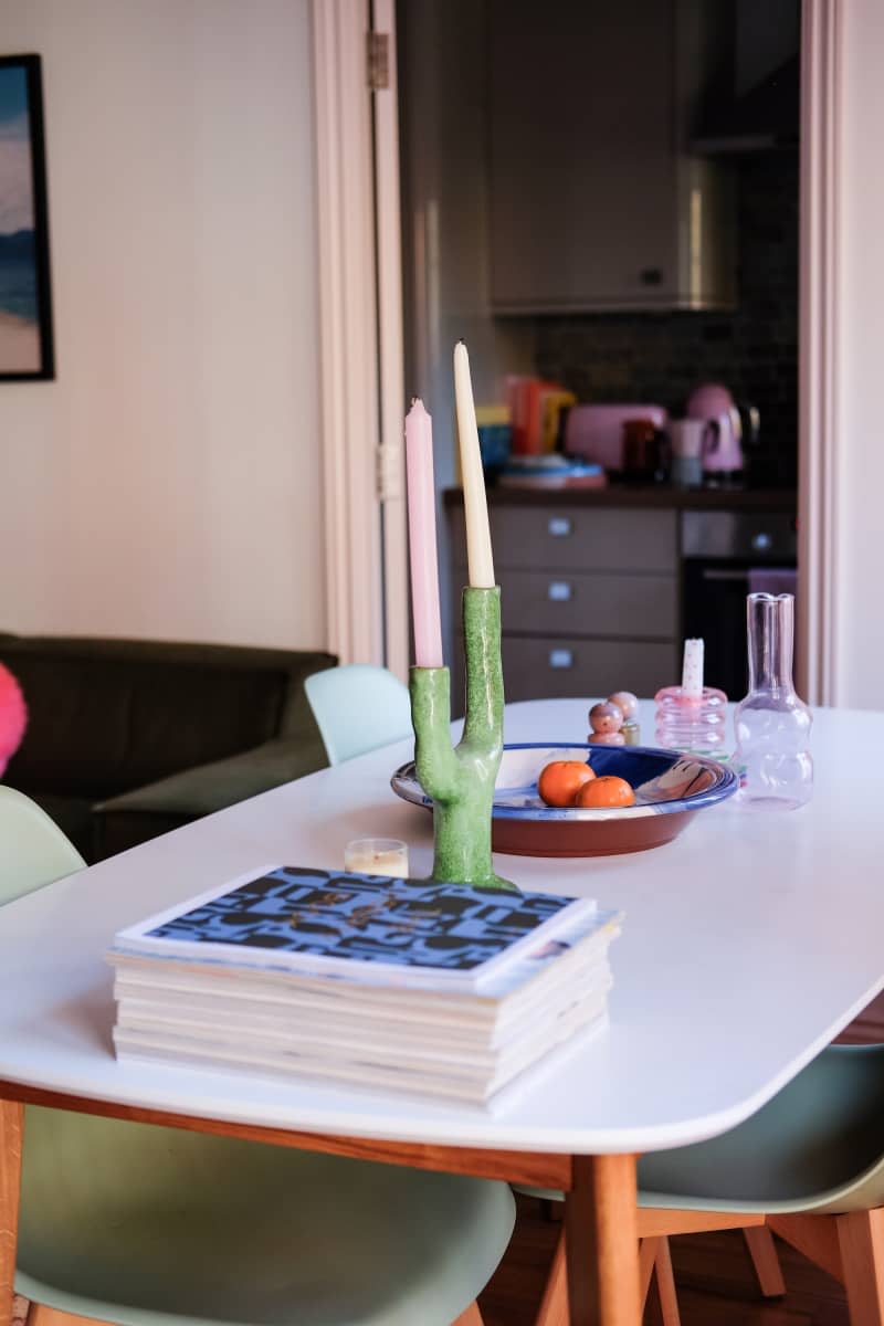 Candles sit atop white dining table in neutral toned room.