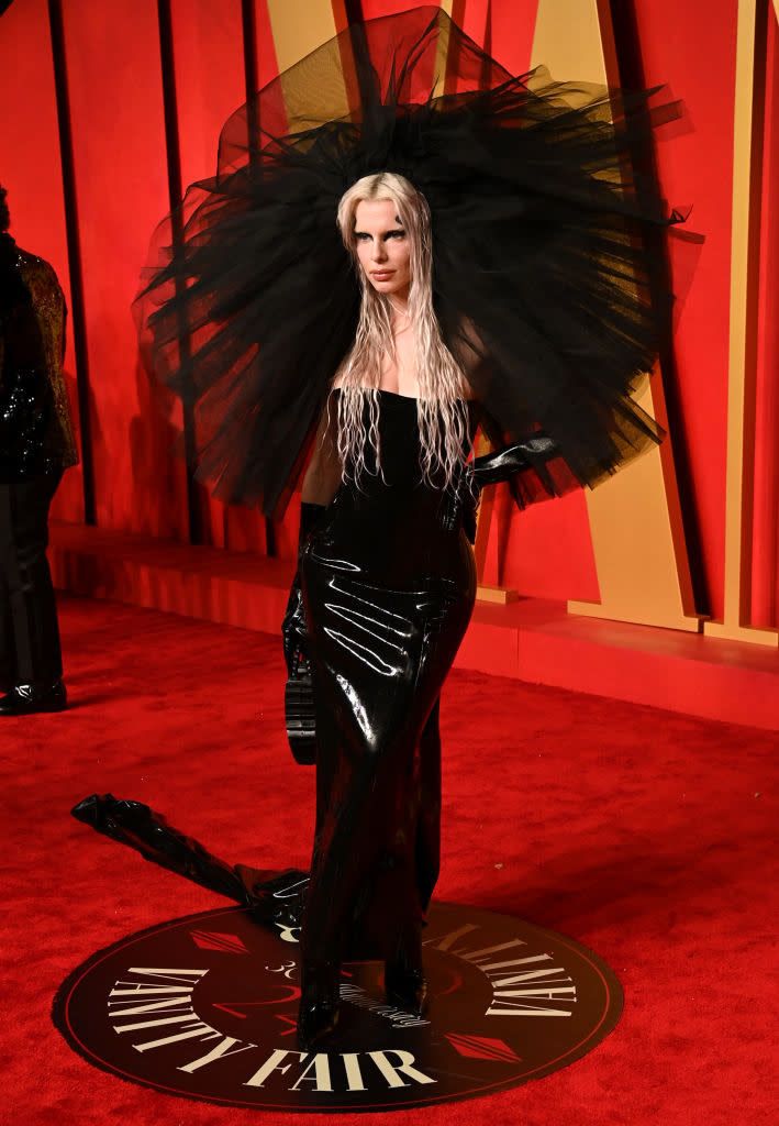 Person on red carpet in a black outfit with voluminous sheer headpiece