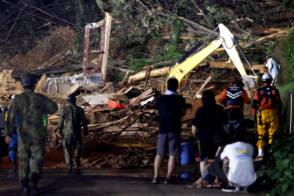 People watch a search operation at the site of a mudslide in Ashikita town, Kumamoto prefecture, southwestern Japan, Saturday, July 4, 2020. Heavy rain triggered flooding and mudslides on Saturday as more than 75,000 residents in the prefectures of Kumamoto and Kagoshima were asked to evacuate following pounding rains overnight. (Kyodo News via AP)