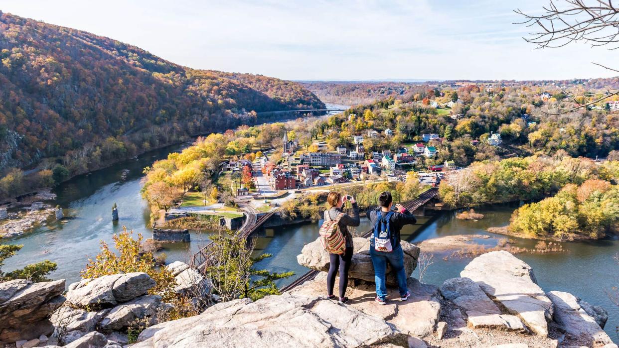 Harper's Ferry, USA - November 11, 2017: Overlook with hiker people women couple, colorful orange yellow foliage fall autumn forest with small village town by river in West Virginia, WV.