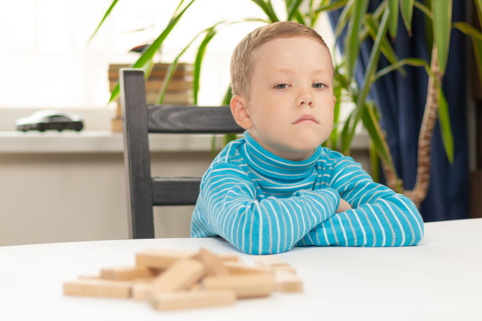 A serious seven-year-old child boy playing games at home at a white wooden table against the background of a light window. (Getty Images)