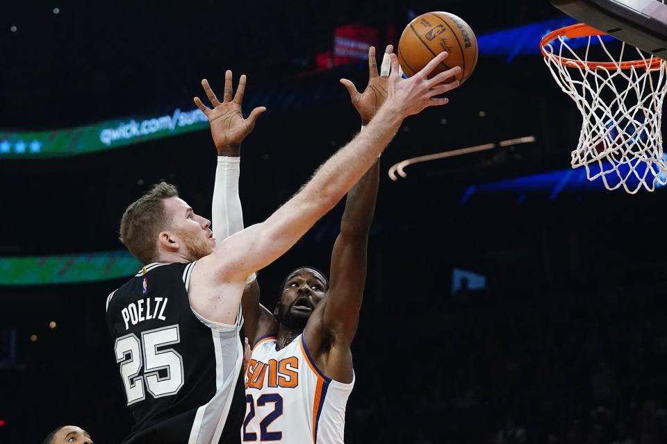 San Antonio Spurs center Jakob Poeltl (25) drives past Phoenix Suns center Deandre Ayton (22) to score during the first half of an NBA basketball game Monday, Dec. 6, 2021, in Phoenix. (AP Photo/Ross D. Franklin)