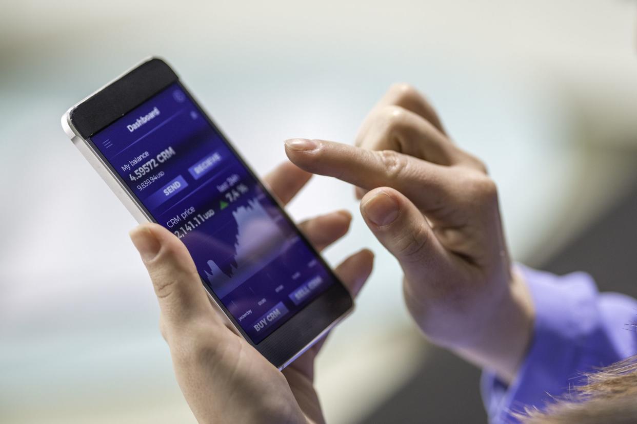 Close-up photo of a woman buying cryptocurrency through a smart phone app that is also showing the growth graph.