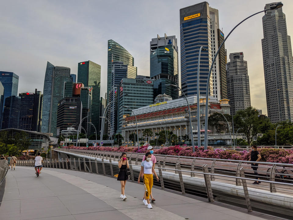 May 2020. Singapore. Scene of everyday Singapore during the world pandemic of 2020 Coronavirus / COVID - 19 people walking with masks one and exercising while a architectural marvel stands in the background (The Esplanade Theater) aka the Durian. A woman puts on a red facemask while walking with her friends.